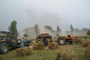 A field with tractors working in a dusty environment.