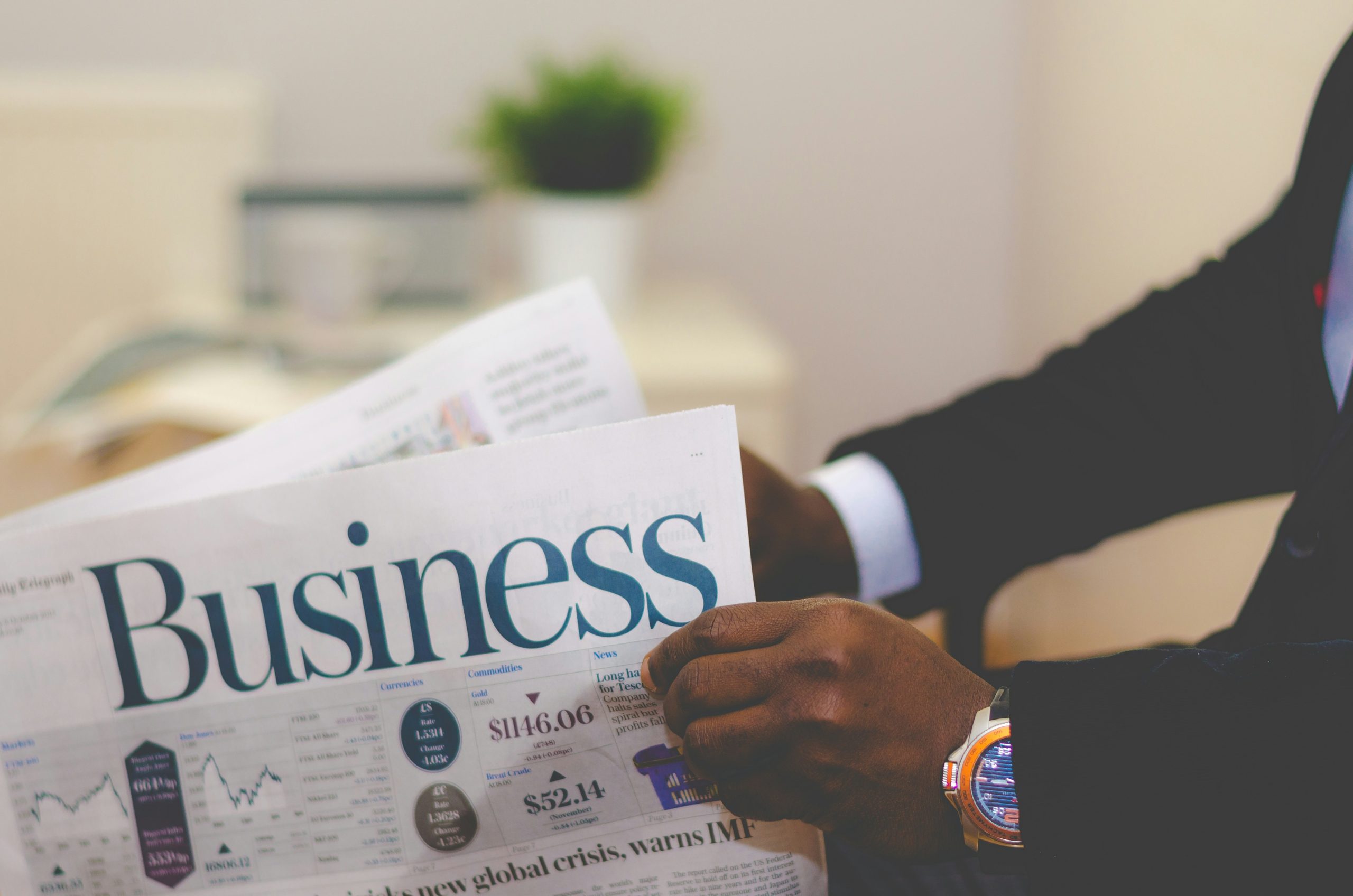 A person reading a business newspaper with financial charts visible.