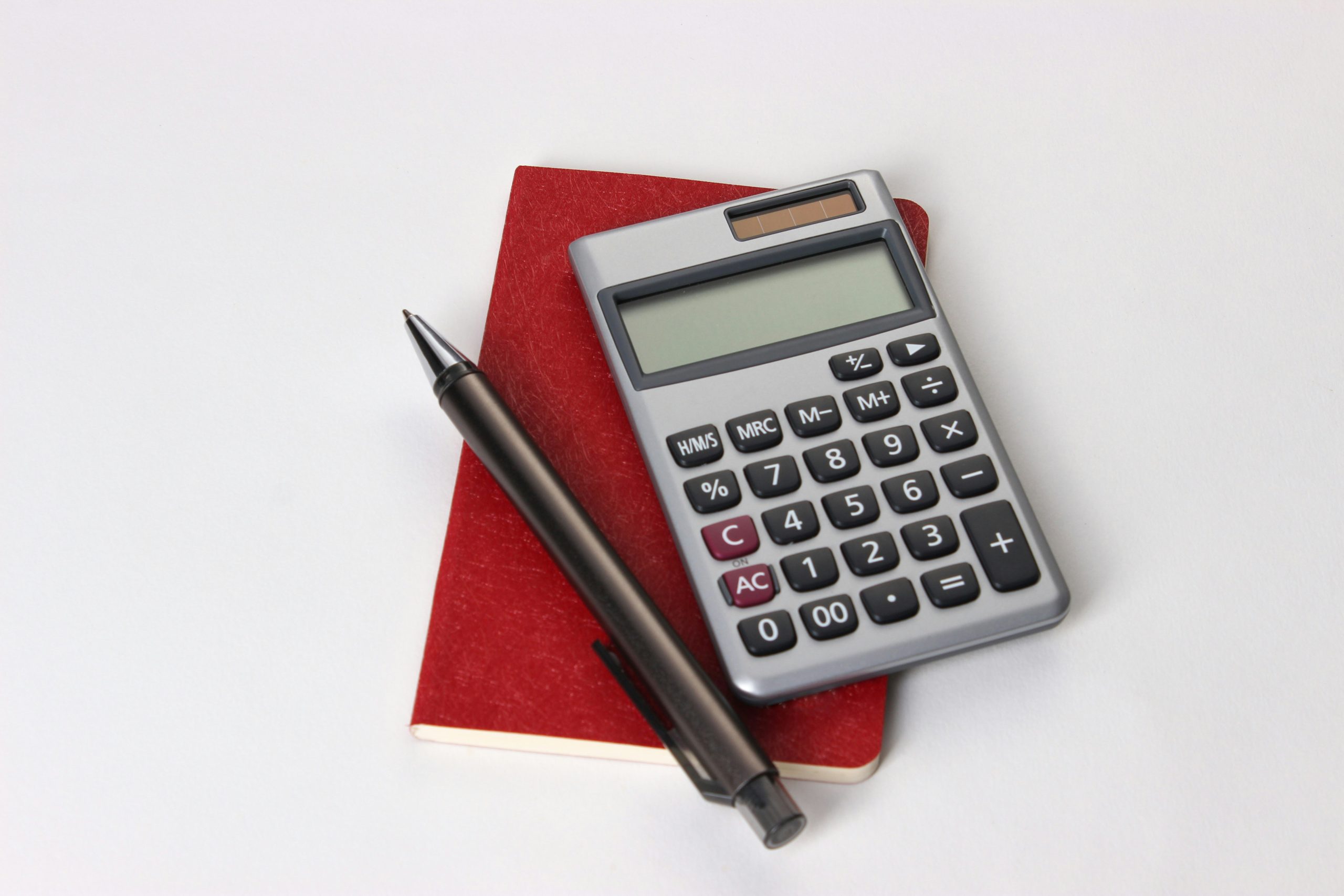 A calculator with a pen and red folder on a white surface.