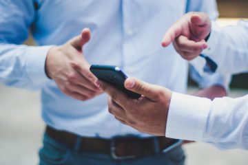 A person in a blue shirt holding a smartphone while discussing something.