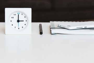 A white desk with a clock, pen, and tax documents.