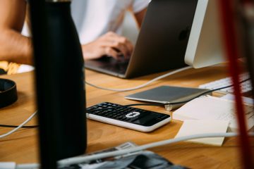 A busy office desk with a calculator, pen, and financial documents.