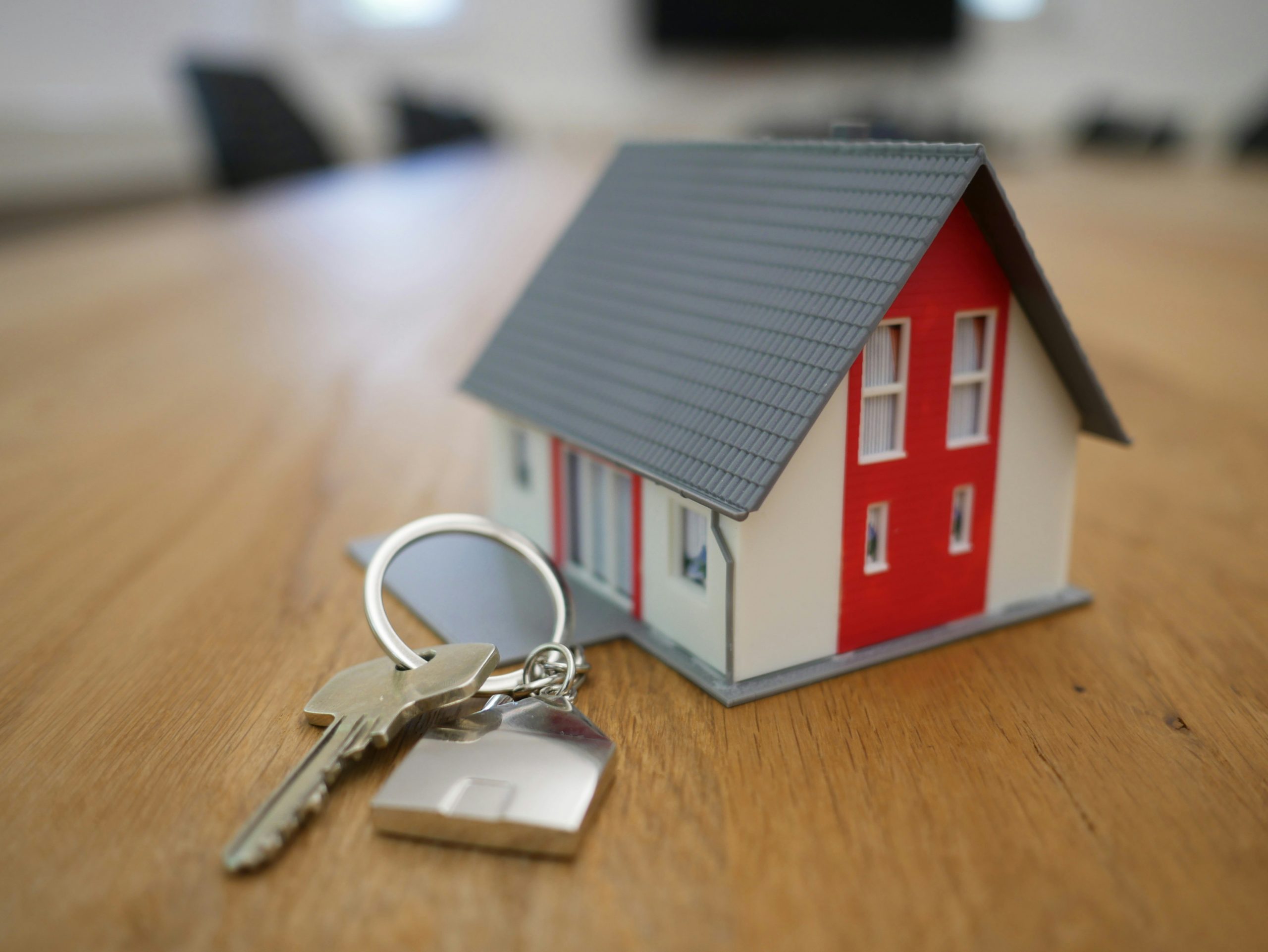 A miniature house model with keys on a wooden table.